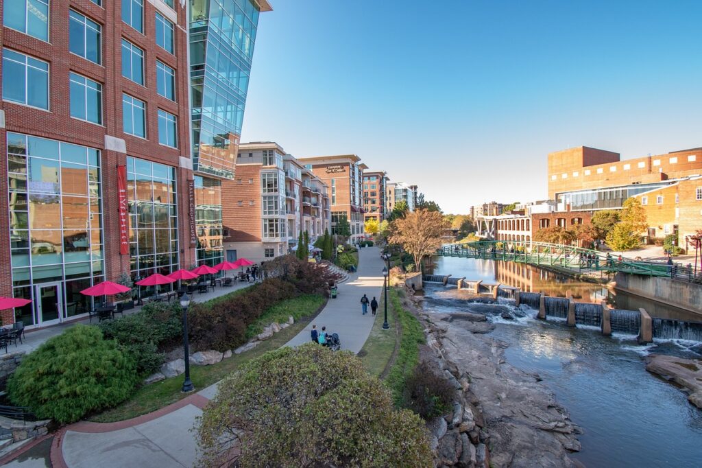 A small river with an arched pedestrian bridge over it courses through a downtown area, shadowed by a tall building