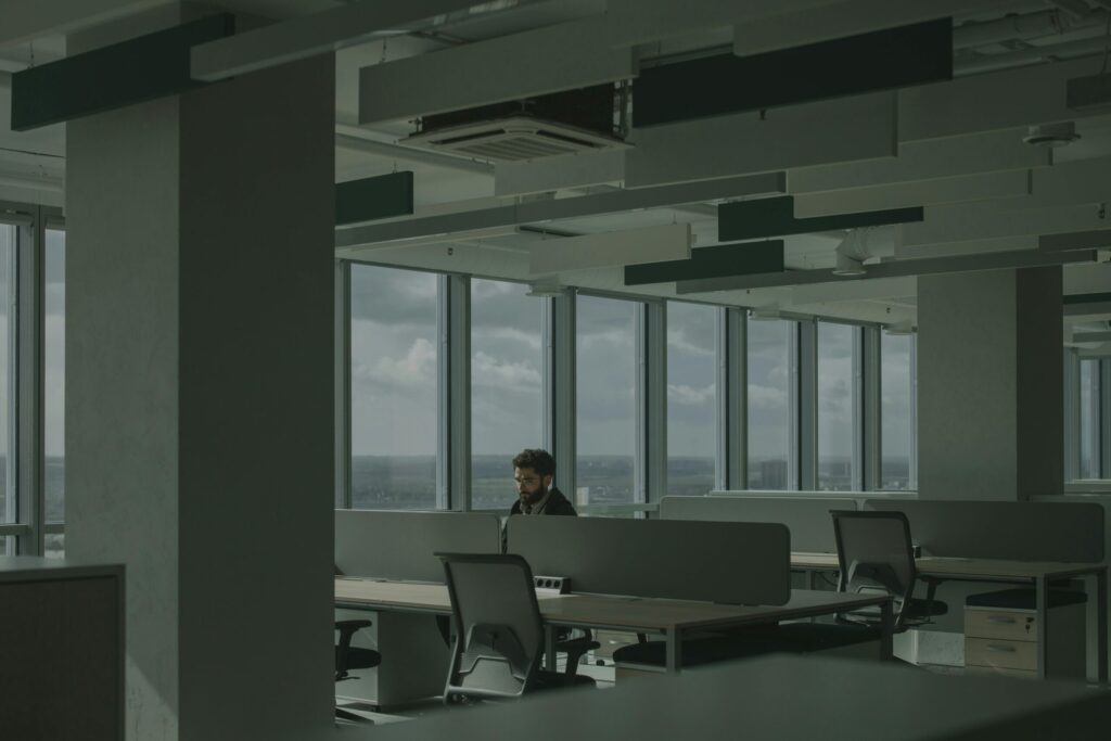A lone office worker in a cubicle with windows behind them.