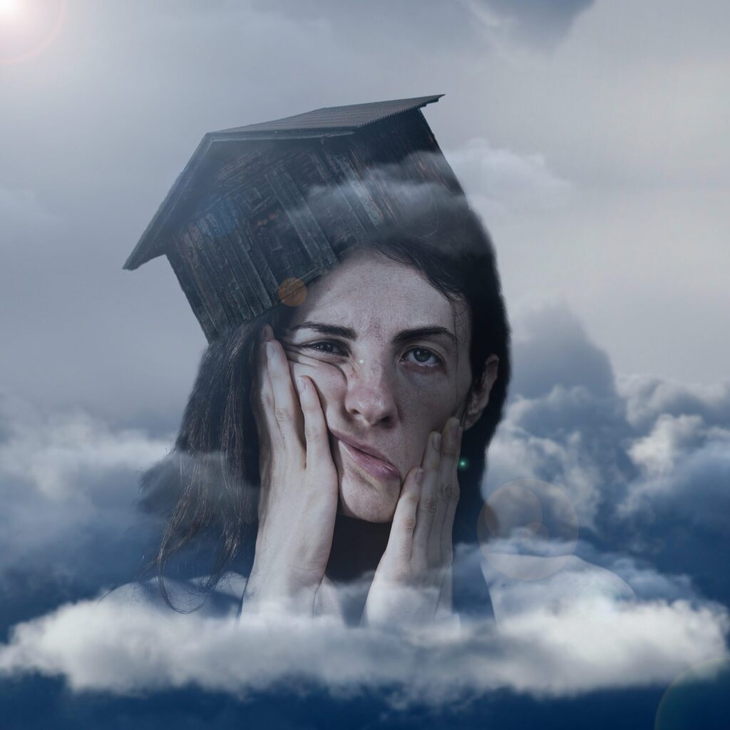 A light skinned woman smushes her face with her hands in agony while looking through a window that is reflecting clouds.