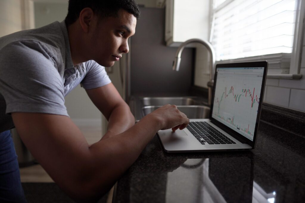 A medium-skinned man uses the track pad of a laptop on a kitchen counter.